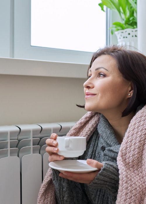 Winter season, woman warming up near home heating radiator